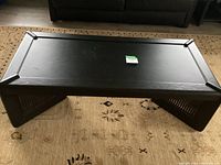 Front view of the black coffee table showing the top surface, framing on edges, and angled lattice side panels.