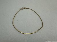 Photo of a delicate 10K gold bracelet laid flat on a grey surface showing the entire bracelet including the clasp.