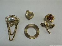 Four assorted jewelry pins and brooches laid out on a flat surface, showing details of each item clearly.