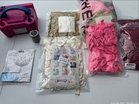 Lot contents showing the pink electric balloon pump, assorted bags of balloons in gold, pink, and red, spool of balloon ribbon, and a pack of confetti balloons.