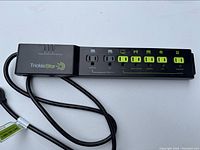 Black TrickleStar power bar with six outlets, green sliding control switches on four outlets, one always-on outlet, and light sensor area on the left end.