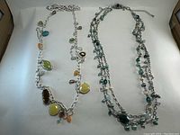 Photo showing both Lia Sophia necklaces on a white background. One necklace is large linked chain with various multicolor polished stone pendants. The other necklace is multi-strand with small colored beads.