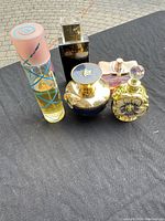 Five assorted perfume bottles arranged on a black surface outdoors, visible full set and design details