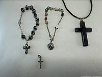 Full lot showing black hematite cross necklace on black cord, two beaded religious bracelets with cross and shell charms, and a silver crucifix charm