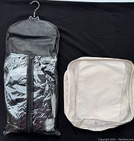 Black hanging bag with clear front zipper and metal hook, and beige mesh packing cube shown on black background.