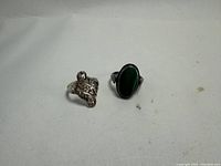 Two vintage 925 sterling silver rings shown side by side, one with a large textured design, the other with an oval green stone.