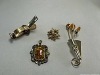 Four vintage amber jewellery items arranged on a grey surface: a floral brooch, a rectangular pendant, a star-shaped pin, and a tie clip with teardrop amber stones.