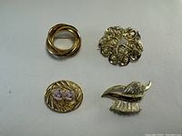 Four vintage brooches and pins displayed on a white background showing a variety of designs including gold-toned loops, rhinestones, enamel flower, and abstract bird shapes.