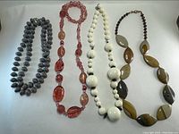 Four vintage costume jewellery necklaces with diverse bead styles and colors on a white background.