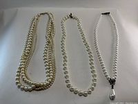 Photo showing three vintage pearl-like necklaces arranged side by side highlighting the styles and pendant detail.