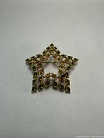 Image showing a vintage Sarah Coventry star-shaped brooch with gold-tone metal and amber-colored rhinestones.