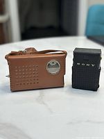 Side-by-side view of two vintage transistor radios in original leather cases, one black Sony and one brown Stradivarius.