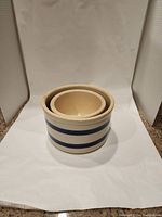 Photo of two nesting stoneware crocks showing front view of both, highlighting blue stripes and nesting fit.