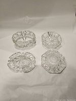 Top view of four crystal pieces including lids and bases showing detailed cut glass patterns and designs.