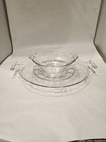 Two clear glass serving dishes stacked; larger round plate with two handles, smaller dish also with handles.