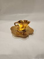 Small gold-colored scalloped teacup with matching tray on a neutral background angled to highlight the cup handle.