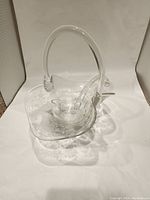Front angled view showing the basket's clear glass, floral etching on sides, and curved handle attached at two points.
