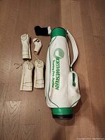 White and green Northwestern Touring Pro Junior golf bag next to five golf club covers including numbered and putter covers, placed on wooden floor.