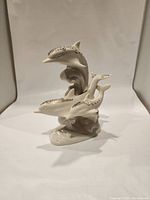 Front view of the cream porcelain dolphin figurine with stylized waves and gold/black highlights.