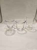 Three clear glass Imperial Candlewick cups shown side by side with beaded bases and handles where applicable.