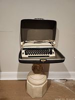 Full view of the Sears electric typewriter sitting inside its hard carrying case, with power cord coiled on top. The case is open showing interior and product size.