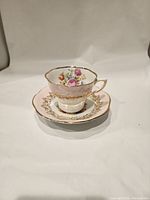 Side angle of tea cup on matching saucer displaying pink band and floral pattern inside cup