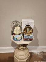 Three snowglobes displayed on a pedestal including Lincoln Memorial, Twin Towers parade, and New York City parade scenes.