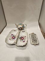 Overall view of three vintage porcelain items including a teapot, divided serving tray, and toast rack on a white backdrop.