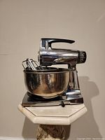 Front angle view of vintage Sunbeam Mixmaster chrome stand mixer with black handle, stainless steel bowl with beaters inside.
