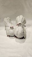 Front view of two white porcelain love bird figurines showing detailed feathers and gentle pink coloring on beaks and feet.
