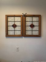 Front view of two antique stained glass windows mounted side by side on a wall showing textured clear glass and red diamond detail.