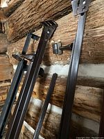 Three metal bed frame components leaning against a rustic wood wall, showing vertical posts with mounting brackets for mattress support.