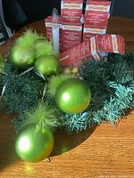 The 17-inch faux spruce wreath decorated with green feathered ornaments and Sylvania electric sensor candle boxes arranged on top.