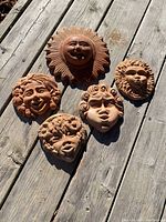All five clay garden décor faces arranged on wooden planks, showing variety of facial expressions and size