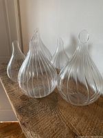 Six clear glass teardrop-shaped vases with ribbed swirl pattern, two smaller and four bigger, arranged on a wooden surface.