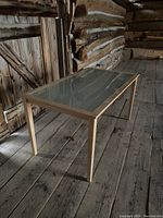 Full view of rectangular IKEA dining table with wood frame and frosted glass top in rustic wooden floor room.