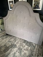Side angle showing grey fabric tufted queen size headboard with curved top and missing one foot
