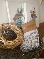 Two herb-themed 11x14 canvas prints shown propped against a wall with herb-themed pillow cover and natural twig bowl in front.