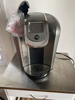 Front side view of silver and black Keurig 2.0 coffee maker with water reservoir on side and display panel on front top