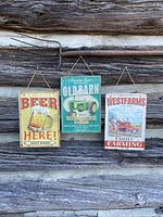 Three vintage metal signs hanging on a wooden wall, approximate size 7x10 inches. Signs include a beer advertisement, an old barn farm tractor sign, and a WestFarms family farming tractor sign.