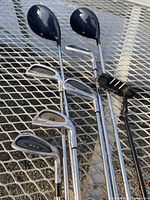 Photo showing two wood drivers, four irons, and a putter arranged on a metal grid surface
