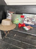 The lot items displayed on a black wooden surface including the outdoor hat, three books, hummingbird feeder, and nectar packet.