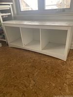 Front angle showing white storage bench with scratches and three open cubby sections