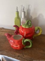 Photo showing the hot pepper-themed ceramic teapot and creamer alongside two kitchen bottles, one green and one white.