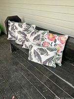 Four throw cushions arranged on an outdoor bench, showing various leaf and floral patterns and sizes.