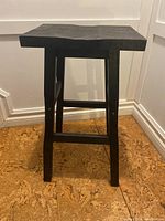 Front view of black painted wood bar stool showing rectangular seat, four legs with cross support, and scratches on paint.