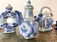 Front angle of all three blue and white hand painted teapots showing various shapes and detailed designs, placed on decorative silver tray.