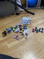 Photo showing the assortment of figures spread on the floor with a small white carrying case with colored dots.