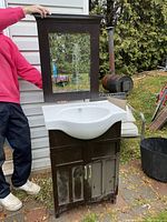 Bathroom vanity with white ceramic sink and matching framed mirror being held up separately.