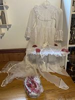Full display of dress on hanger with parasol and basket accessories arranged on table beneath it, veil draped on floor